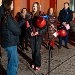Grupa osób uczestniczy w wydarzeniu na świeżym powietrzu. Dwie osoby rozmawiają, trzymając balony, a w tle widać innych uczestników.