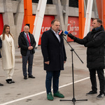 Mężczyzna udziela wywiadu stojąc przed mikrofonem, obok stoi dziennikarz, w tle stoją inni uczestnicy.