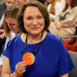 Kobieta w kobaltowej sukience prezentuje otrzymany medal