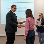 Zastępca prezydenta Tomasz Klim wręcza dokument kobiecie, która stoi naprzeciwko. W tle widać choinkę i flagę. Obok stoi inna kobieta z dokumentami.
