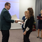 Na zdjęciu odbywa się ceremonia wręczenia dokumentów. Zastępca prezydenta Tomasz Klim i kobieta podają sobie ręce, a w tle widać inne osoby oraz choinkę świąteczną.