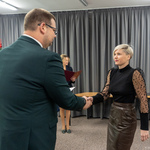Zastępca prezydenta Tomasz Klim i kobieta podają sobie ręce w formalnej atmosferze. W tle widać choinkę i osobę trzymającą dokumenty.
