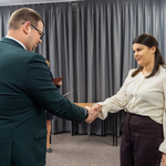 Zastępca prezydenta Tomasz Klim i kobieta podają sobie ręce podczas formalnego spotkania. W tle widać zasłony i inne osoby.