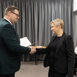 Zastępca prezydenta Tomasz Klim podaje rękę nauczycielce podczas ceremonii wręczenia dokumentów. W tle widać kilka osób siedzących przy stole.