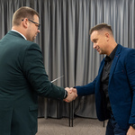 Zastępca prezydenta Tomasz Klim i mężczyzna podają sobie dłonie w formalnej sytuacji, w tle widać kobietę.