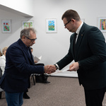 Podczas uroczystości Zastępca prezydenta Tomasz Klim podaje dłoń mężczyźnie.