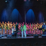 Grupa chórzystów stoi na scenie podczas koncertu.