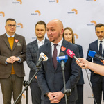 Marszałek Łukasz Prokorym udziela wywiadu podczas konferencji prasowe, w tle stoją inni uczestnicy.