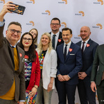 Zastępca prezydenta Rafał Rudnicki robi zdjęcie telefonem razem z uczestnikami konferencji prasowej.