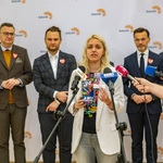 Kobieta udziela wywiadu podczas konferencji prasowej, w tle stoją inni uczestnicy.