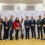 Dziewięciu uczestników konferencji prasowej stoi pozując do wspólnego zdjęcia.