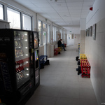 Korytarz, w którym znajduje się automat z przekąskami oraz kawą, w tle: mężczyzna siedzący na ławce