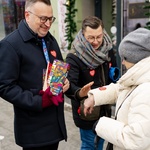Wolontariusze podczas porannej kwesty. Kobieta wrzuca pieniądze do puszki WOŚP