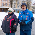 Starsza pani oraz pan pozują do pamiątkowego zdjęcia. Oboje na swoich kurtkach mają naklejone czerwone serduszka WOŚP