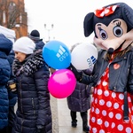 Wolontariuszka ubrana w strój myszki Minnie trzyma w dłoniach kolorowe balony 