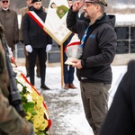 Mężczyzna salutuje trzymając w dłoni duży, biały znicz 