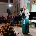 Kobieta ubrana w długą zieloną suknię przemawia do uczestników wydarzenia 