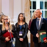 Dwie kobiety oraz mężczyzna ubrani w galowe stroje stoją podczas uroczystości 