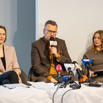Zastępca prezydenta Rafał Rudnicki mówi do mikrofonu podczas konferencji prasowej, przy stole siedzą dwie kobiety.