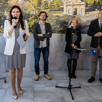 Uczestnicy konferencji stoją, prowadząca Urszula Boublej mówi do mikrofonu.