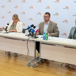 Troje uczestników konferencji prasowej siedzi przy stole.