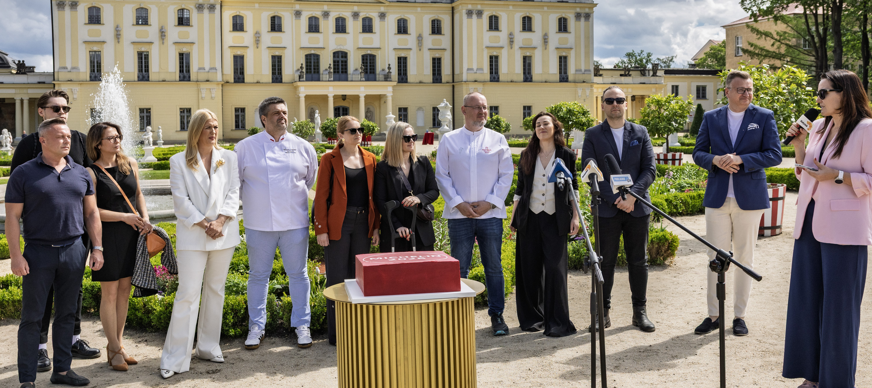 Uczestnicy konferencji stoją w Ogrodzie Branickich, na pierwszy planie stoi tort na stoliku.