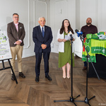 Uczestnicy konferencji prasowej stoją w sali, na środku stoi mikrofon.