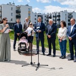Uczestnicy konferencji stoją za mikrofonami, w tle zieleń i zabudowania.