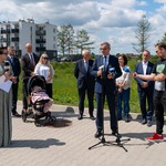 Mężczyzna stoi przed mikrofonami, w tle stoją inni uczestnicy konferencji prasowej.