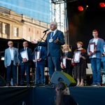 Prezydent Tadeusz Truskolaski przemawia do mikrofonu podczas uroczystości, w tle stoją nagrodzeni.