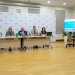 Uczestnicy konferencji siedzą przy stole, obok stoi monitor z wyświetlaną grafiką.