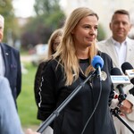Kobieta udziela wywiadu stojąc przed mikrofonami.