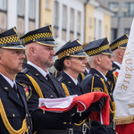 Funkcjonariusze Straży Miejskiej stoją w szeregu, jeden z nich trzyma flagę w rękach.
