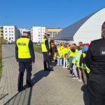 Uczniowie w kamizelkach odblaskowych stoją w dwurzędzie na tle szkoły, obok dwóch policjantów oraz strażniczka miejska