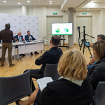 Uczestnicy konferencji prasowej siedzą w dużej sali podczas spotkania.