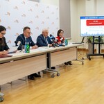Uczestnicy konferencji siedzą przy stole, w tle stoi monitor z wyświetlaną prezentacją.