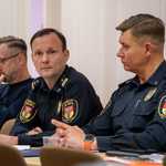 Funkcjonariusze Straży Miejskiej siedzą przy biurku podczas spotkania.