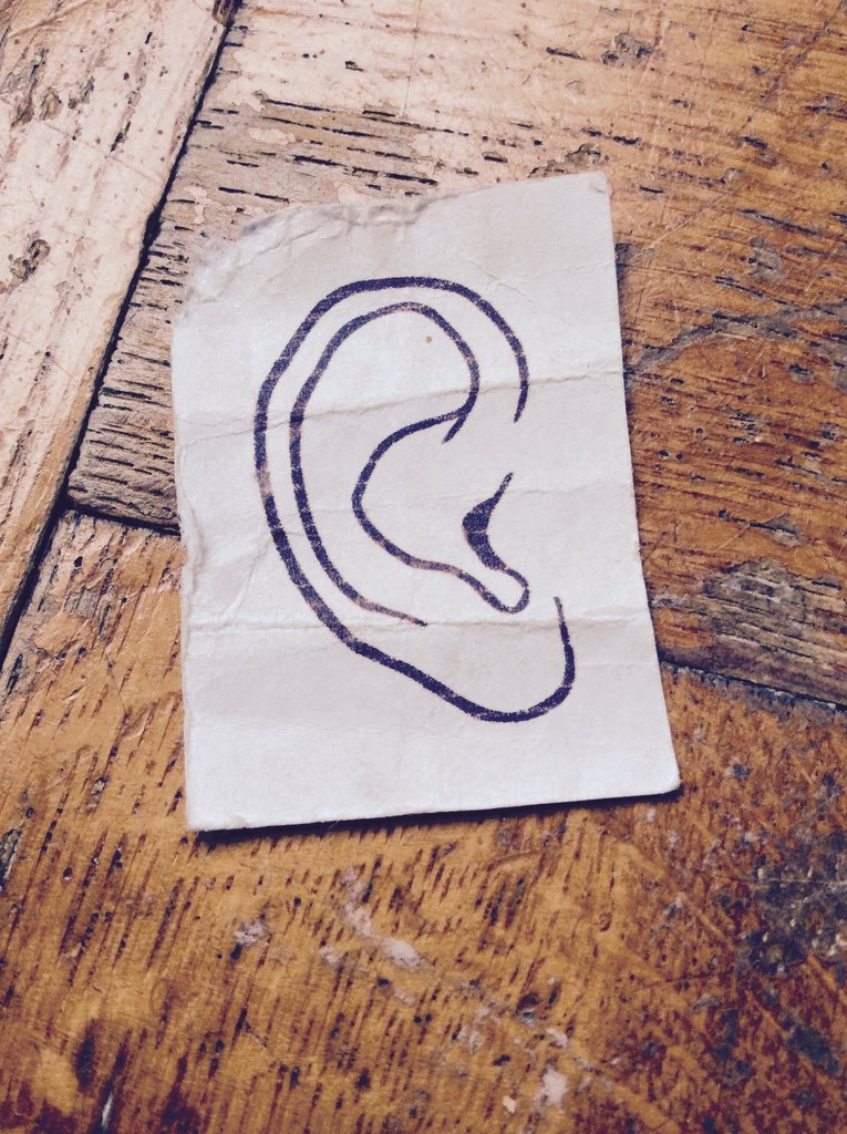 Kartka z naszkicowanym uchem leżąca na parkiecie