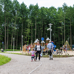 Mieszkańcy spacerują, w tle plac zabaw dla dzieci